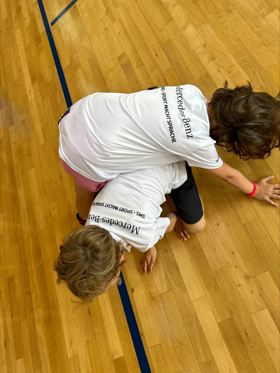 Zwei Kinder ringen auf dem Boden einer Sporthalle miteinander.