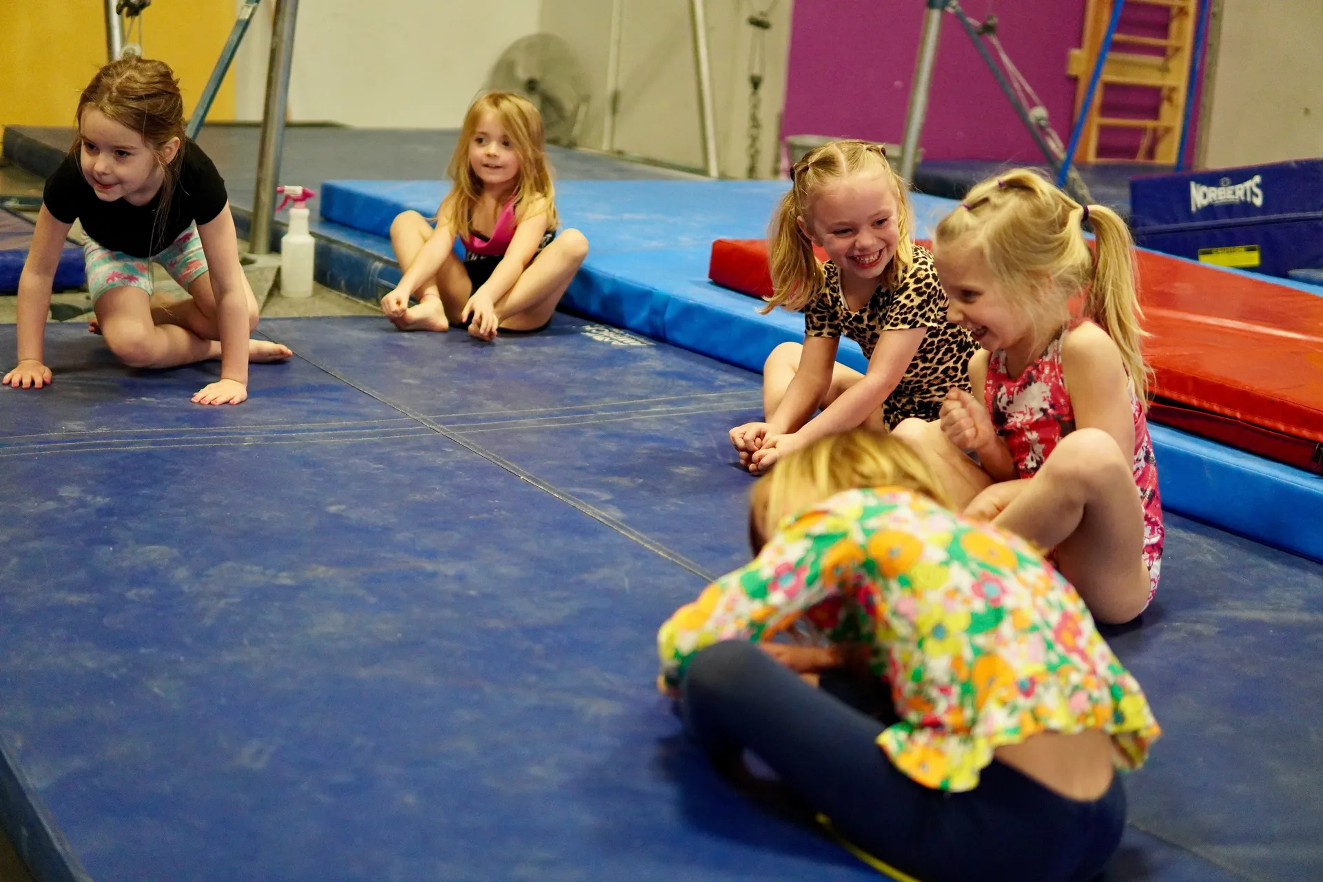 Mehrere Kinder sitzen und spielen auf Matten in einer Turnhalle.